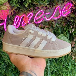 Tênis Adidas Campus 00s em camurça cinza com detalhes em branco e listras brancas. Solado off white com detalhe caramelo, modelo de primeira linha, ideal para treinos, passeios e looks casuais. Disponível na Maiara Valentina Moda Feminina.